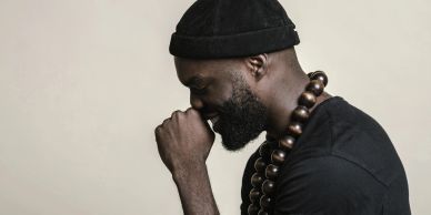 Profile of a thoughtful man wearing a beanie and wooden bead necklace.